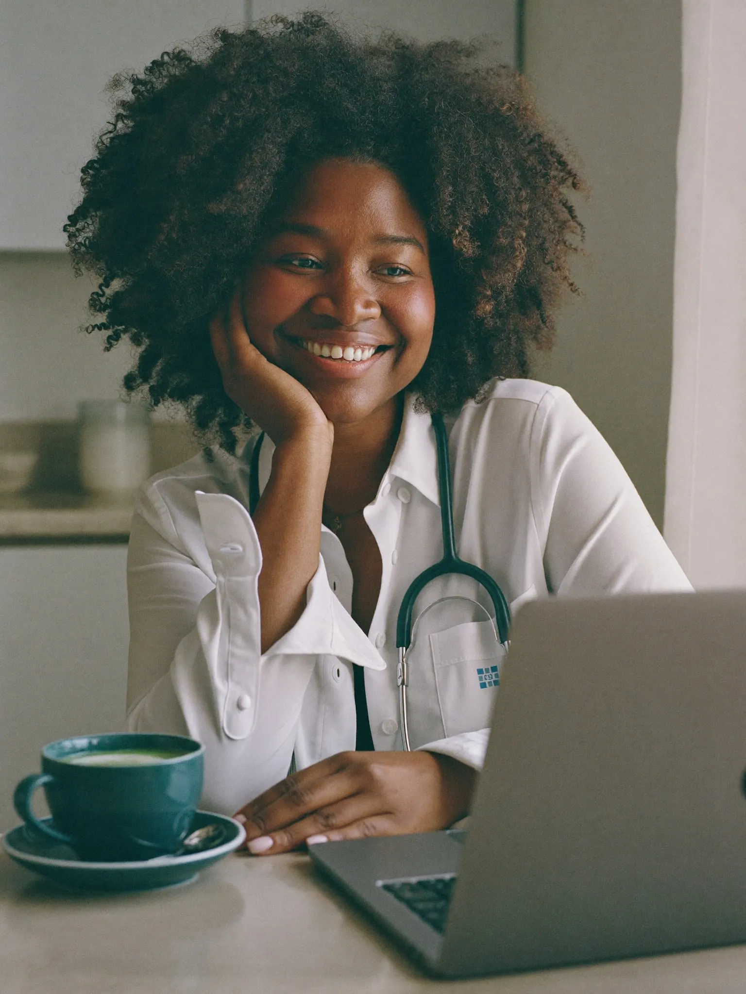A woman at her kitchen table smiling during a video visit on her laptop