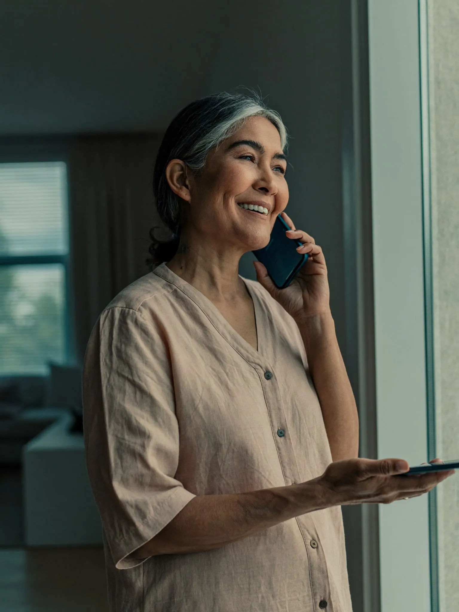 A woman by a window holding a phone during a video visit